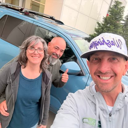 Justin celebrating with customers beside their blue SUV