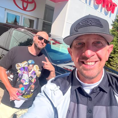 Justin wearing his Seahawks cap beside a customer and vehicle